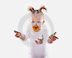 The baby girl with a pacifier in gouache soiled hands and shirt isolated