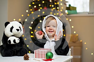 Baby girl in a panda costume with panda toy open Christmas present under the Christmas tree