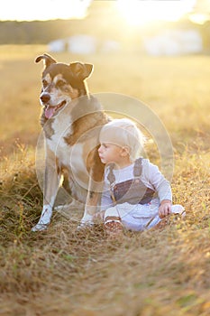 Baby Girl And Pet German Shepherd Dog Relaxing on Farm at Sunset