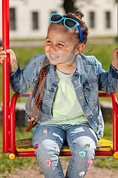 Baby girl with pigtails and sunglasses sits on a swing