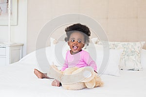 Baby girl in pink babygro sitting on bed