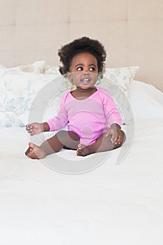 Baby girl in pink babygro sitting on bed