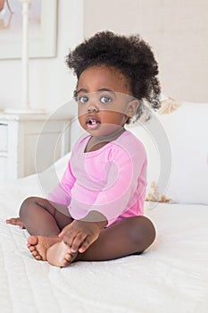 Baby girl in pink babygro sitting on bed photo