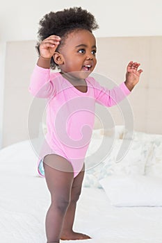 Baby girl in pink babygro standing on bed