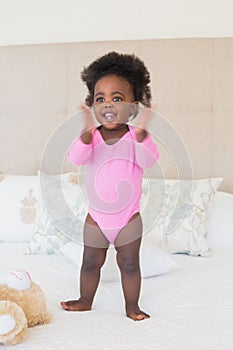 Baby girl in pink babygro standing on bed photo