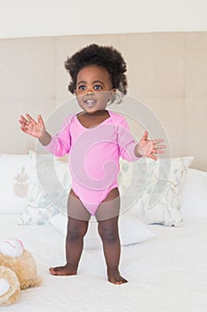 Baby girl in pink babygro standing on bed photo