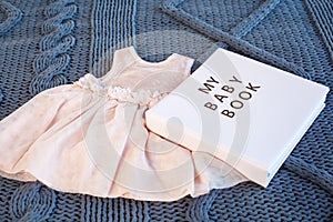 Baby girl pink dres clothes with newborn book album on blue knitting plaid background