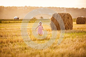 Baby girl pink dress stand on stack wheat field