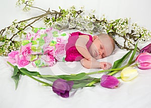 Baby girl in pink inside of basket with spring flowers.