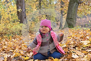 Baby girl in pink warm coat sitting on the ground