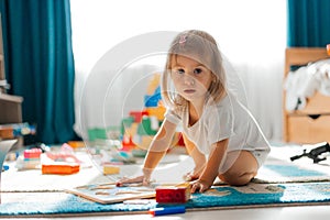 Baby girl playing indoors sitting on floor in playroom at home with constructor. Educational game for baby and toddler