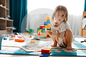 Baby girl playing indoors sitting on floor in playroom at home with constructor. Educational game for baby and toddler