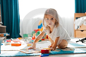 Baby girl playing indoors sitting on floor in playroom at home with constructor. Educational game for baby and toddler