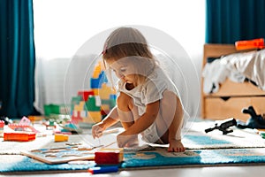 Baby girl playing indoors sitting on floor in playroom at home with constructor. Educational game for baby and toddler