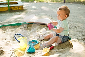 Baby girl playing in sandbox on outdoor playground. Child with colorful sand toys. Healthy active baby outdoors plays games