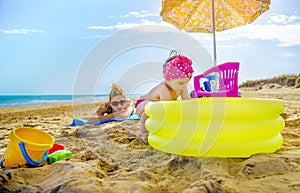 Baby girl plays yellow inflatable pool mom checks her sunbathing on beach towel