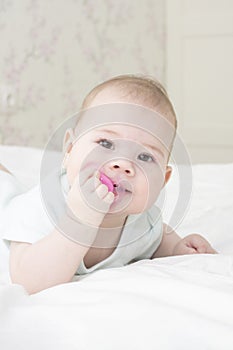 Baby girl portrait close-up vertical. The baby`s face is 6 months old, lying on his stomach, pulling the nipple in his mouth