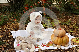 Baby girl posing with pumpkin and toys among trees in autumn par