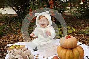 Baby girl posing with pumpkin and toys among trees in autumn par