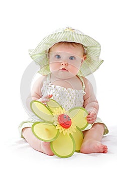 Baby girl in pretty hat plays with toy flower