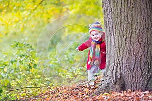 Baby girl in red coat hiding behind big old