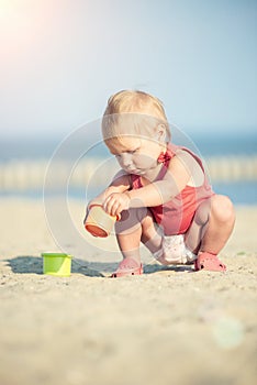 Baby girl in red dress playing on sandy beach near the sea.
