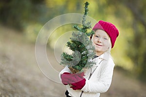 Baby Girl In Red Mittens and Cap Holding Small Christmas Tree