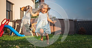 Baby girl running with beagle dog in garden on summer day. Domestic animal with children concept