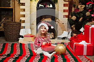 Baby girl Santa`s helper holding present. Shopping sale. Luxury New Years interior. Happy little smiling girl with