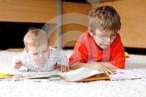 Baby girl and school kid boy reading books at home.