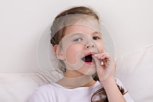 Baby girl sits in bed and checks, shakes her milk tooth