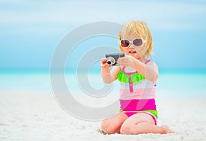 Baby girl sitting on beach and using photo camera