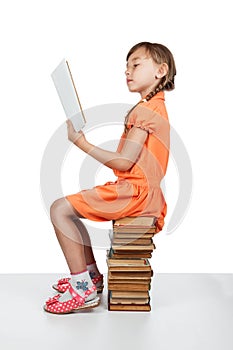 Baby girl sitting on books reading a book