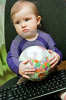 Baby girl sitting with computer keyboard and a globe