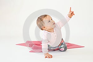 Baby girl sitting on floor isolated over white background pointing