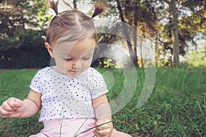 Baby girl sitting in grass in park touching playing and exploring nature - Cute kid toodler outside enjoying the summer