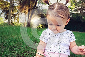 Baby girl sitting in grass in park touching playing and exploring nature - Cute kid toodler outside enjoying the summer