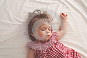 Baby girl sleeping on back with open arms and without pacifier in a bed with white sheets. Peaceful sleeping in a bright