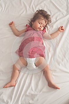 Baby girl sleeping on back with open arms and without pacifier in a bed with white sheets. Peaceful sleeping in a bright