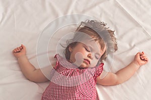 Baby girl sleeping on back with open arms and without pacifier in a bed with white sheets. Peaceful sleeping in a bright room.