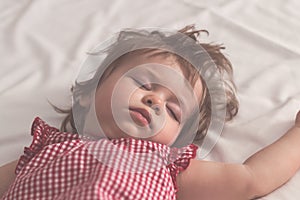 Baby girl sleeping on back with open arms and without pacifier in a bed with white sheets. Peaceful sleeping in a bright room.