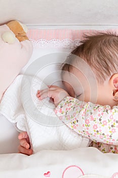 Baby girl sleeping in a cot with pacifier and toy