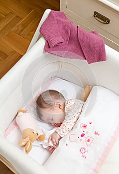 Baby girl sleeping in a cot with pacifier and toy