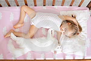 A baby girl is sleeping in a crib with a white cat in the nursery