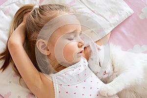 A baby girl is sleeping in a crib with a white cat in the nursery