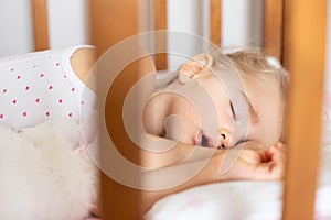 A baby girl is sleeping in a crib with a white cat in the nursery