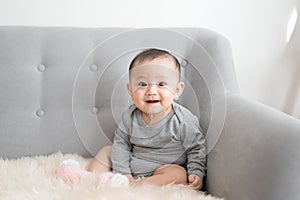 Baby girl is smiling and sitting on sofa in jumpsuit