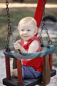 Baby girl smiling and sitting on the swing in the park