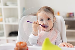 Baby girl with spoon eating puree from jar at home