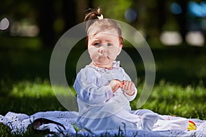 Baby girl in summer dress sitting in the green meadow in the city park.